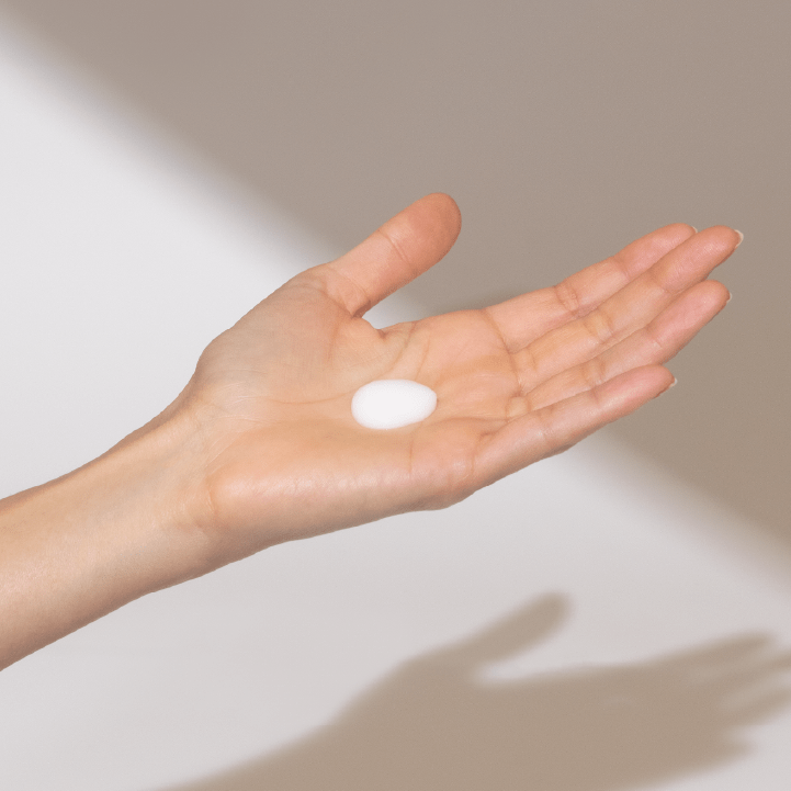 Die Hand einer Frau hält eine Flasche hautberuhigende Feuchtigkeitslotion 60 ml | Feuchtigkeitscreme, reinigt ihre Haut von Unreinheiten und Schmutz.