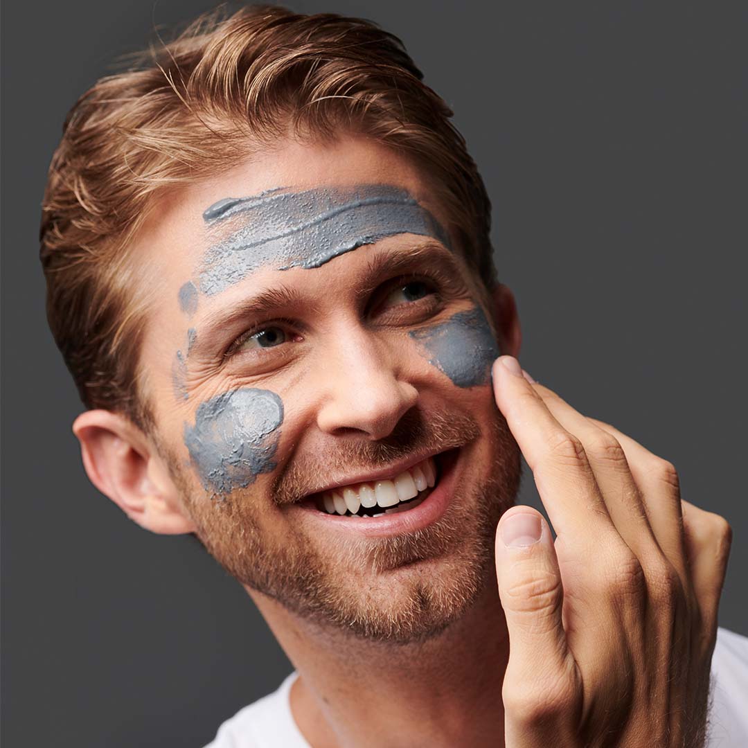 Ein lächelnder Mann mit grauer Gesichtsmaske auf der Haut.