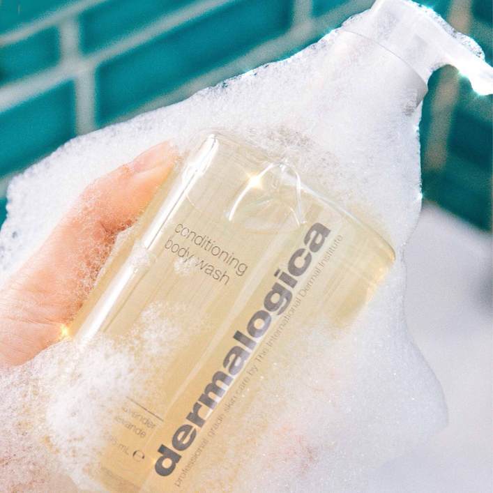 Eine Hand hält eine durchsichtige Flasche mit Dermalogica Conditioning Body Wash umgeben von Schaum.