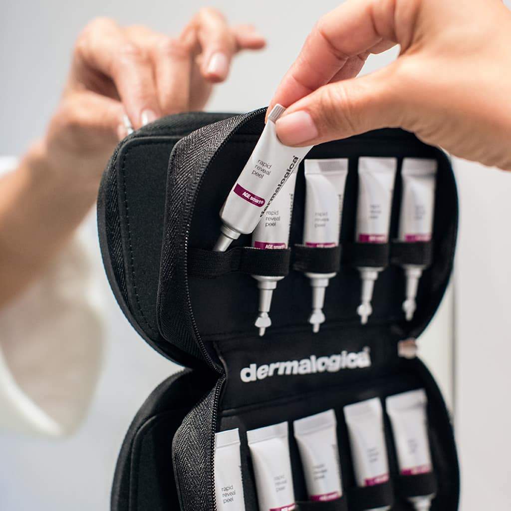 Hände öffnen ein schwarzes -Reise-Set mit mehreren Hautpflegeprodukten.