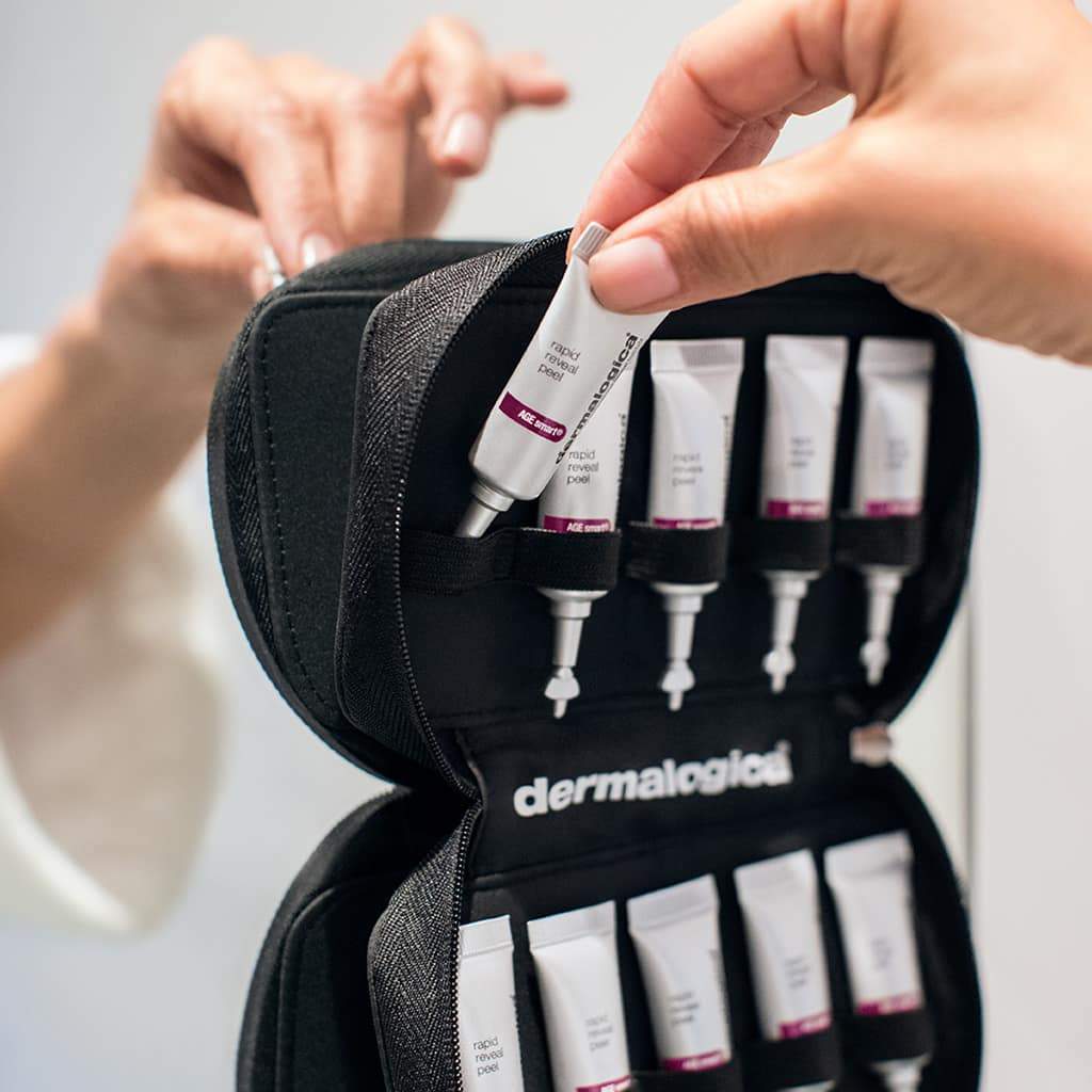 Hände öffnen ein schwarzes Dermalogica-Reise-Set mit mehreren Hautpflegeprodukten.