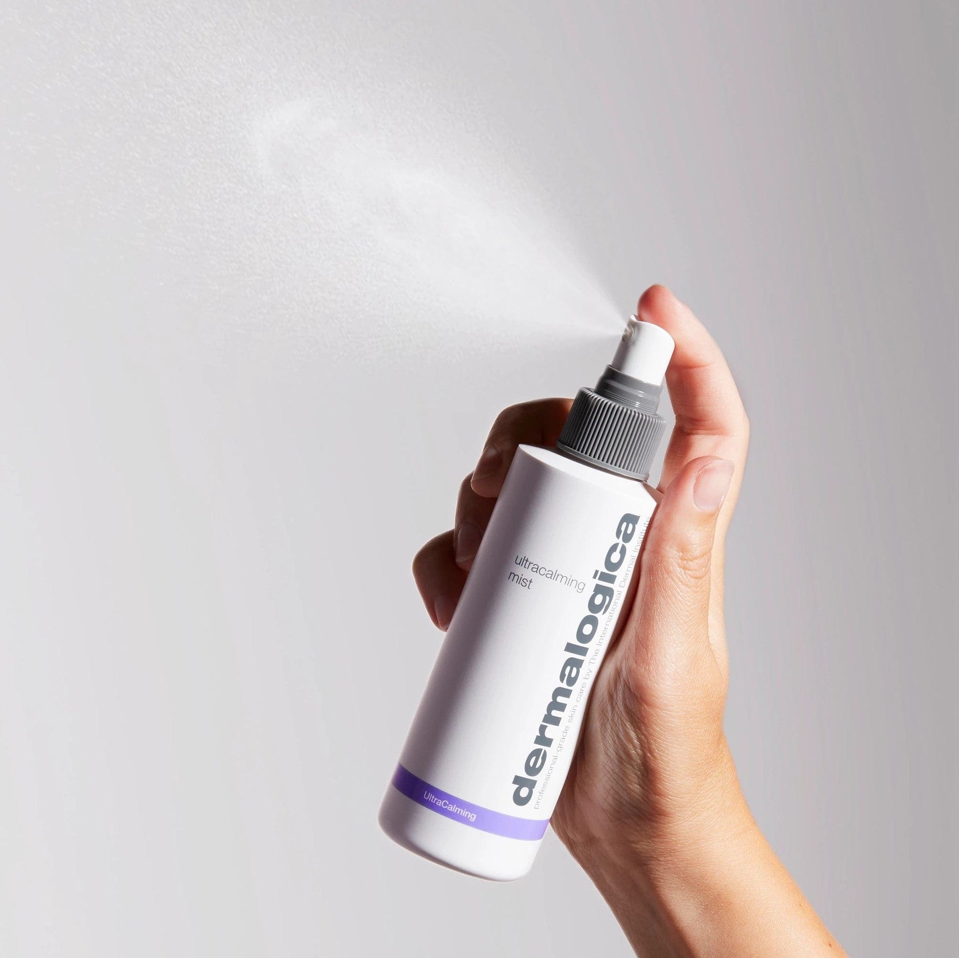 Hand hält eine Flasche Dermalogica Ultracalming Mist, während ein feiner Sprühnebel aus dem Sprühkopf austritt.