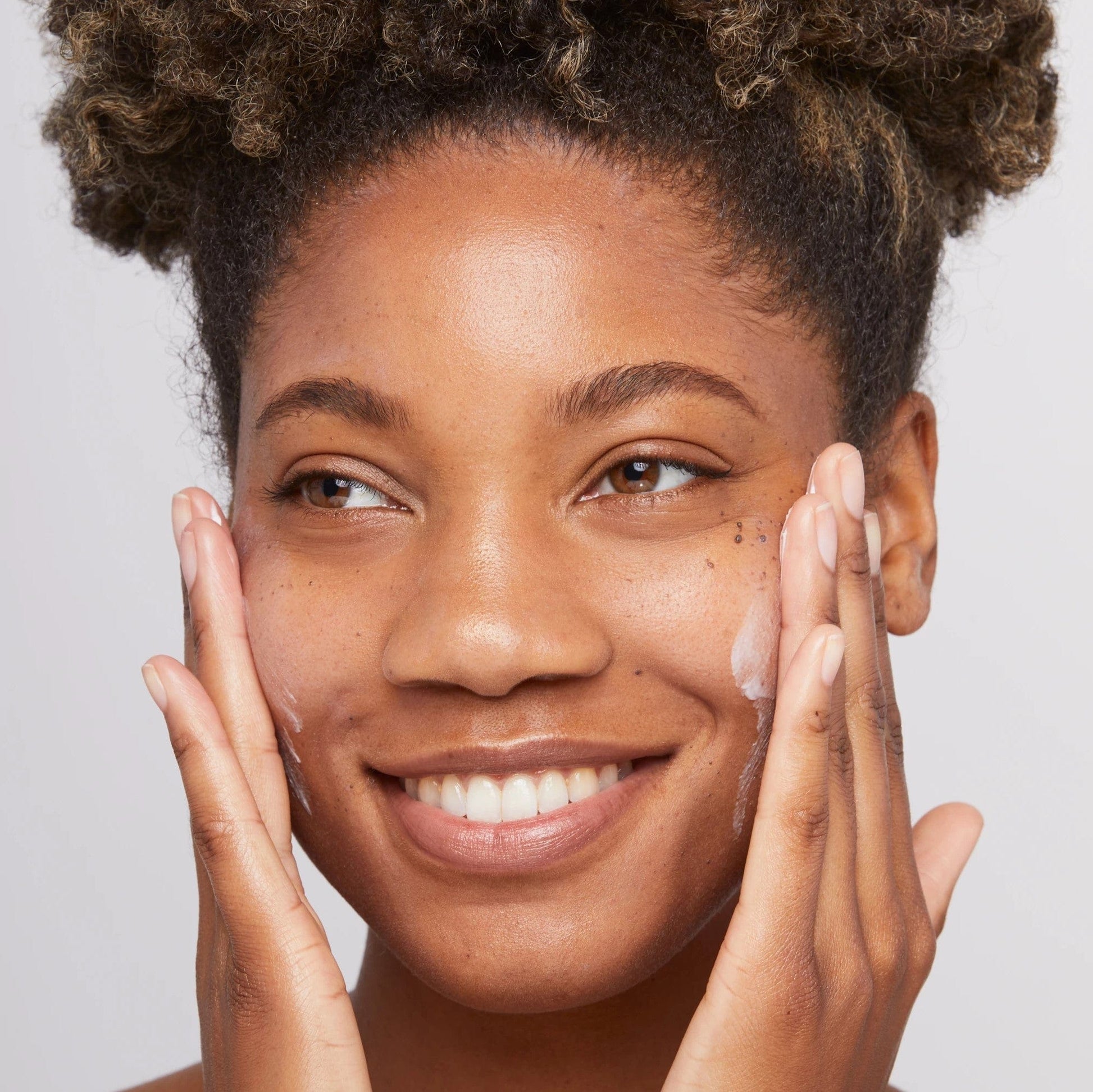 Eine schwarze Frau lächelt mit den Händen im Gesicht und demonstriert die Wirksamkeit der Hautglättungscreme 15 ml | Feuchtigkeitscreme sorgt für eine tiefe Feuchtigkeitsversorgung.