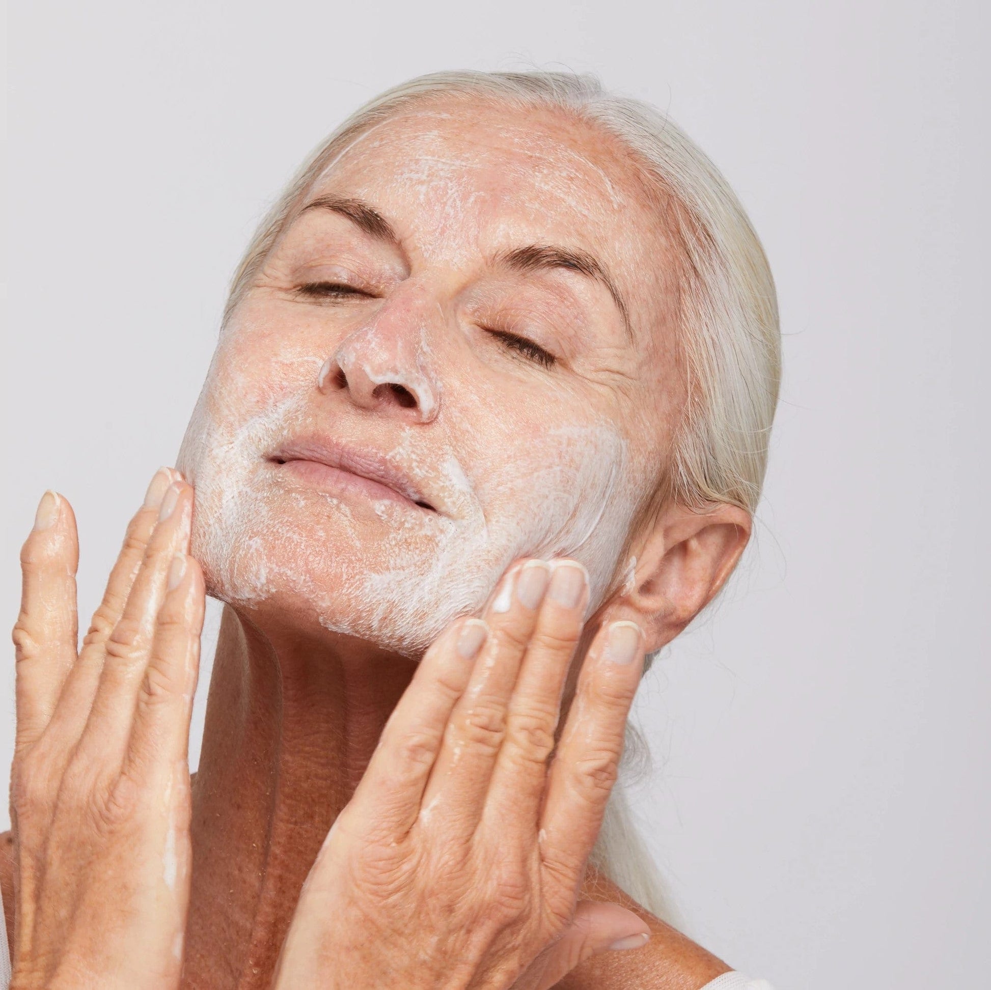 Ältere Frau trägt Gesichtsreinigungsschaum auf ihre Haut auf.