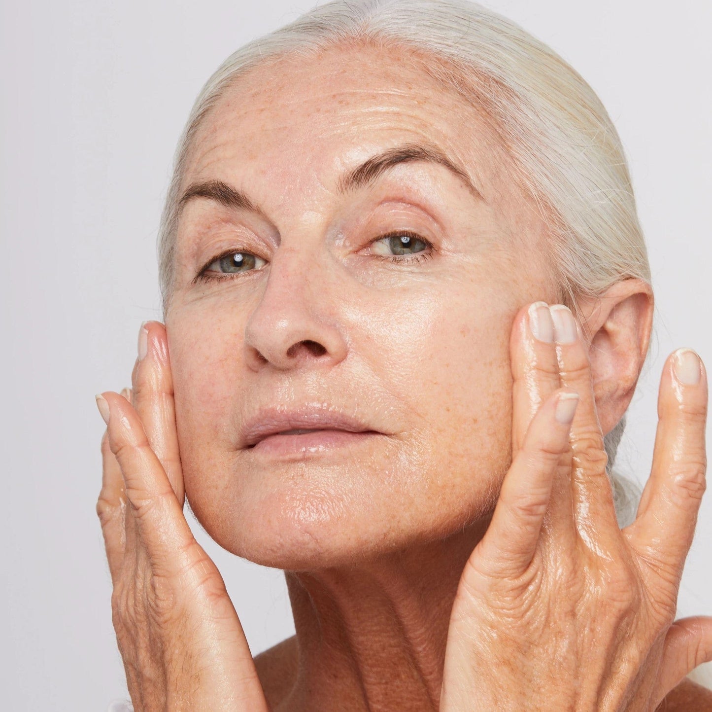 Eine ältere Frau mit den Händen im Gesicht, die Anzeichen von Hautalterung zeigt und nach einer Lösung zur Hautstraffung und -straffung sucht, könnte das Phyto Nature Firming Serum 40ml | ausprobieren Hautstraffendes Serum.