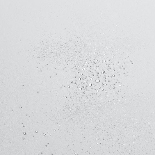 Eine Nahaufnahme von Wassertropfen auf einer weißen Oberfläche mit Ultra Calming Mist 177 ml | Gesichtsspray und gereizte Haut.