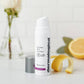 Flasche Dermalogica Dynamic Skin Recovery SPF50 mit offenem Deckel neben Zitronenscheiben und einer Rose im Hintergrund.